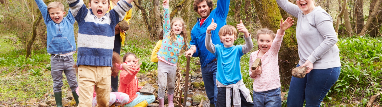 Group of kids and adults in forest raising their hands