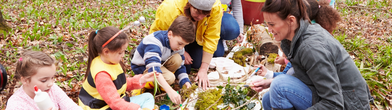 	Group of kids and adults sitting in forest doing crafts with sticks and leaves
